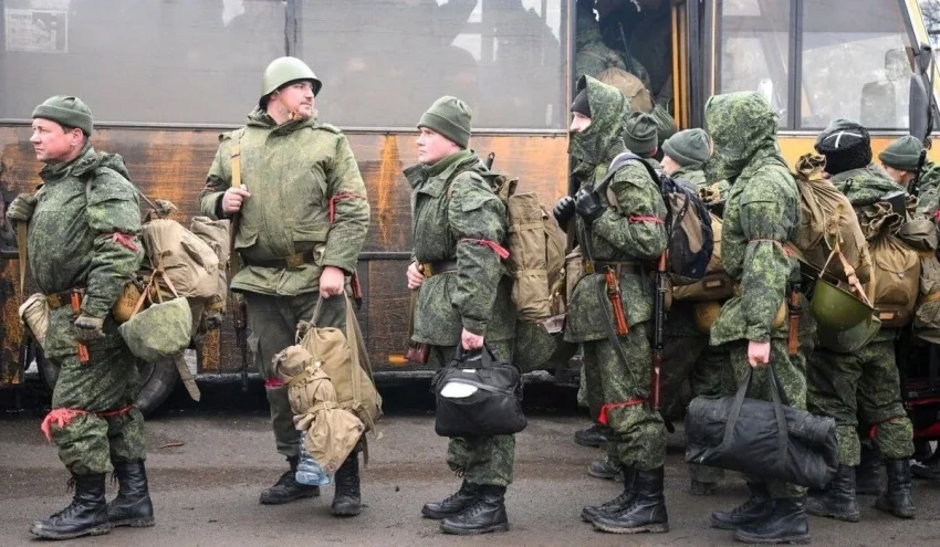 Російські солдати в камуфляжі з речами виходять з автобуса на мобілізацію