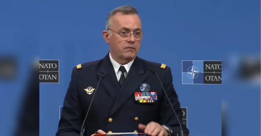 Адмірал у темно-синій уніформі НАТО виступає за трибуною на фоні логотипів Альянсу