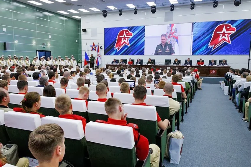 Молодь у червоних футболках слухає виступ військового на великому екрані в залі
